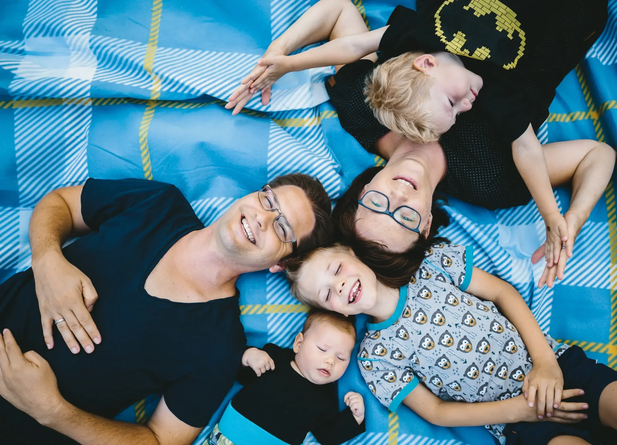 Familie liegt lachend auf einer Picknickdecke im Paradiespark Jena